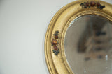 Vintage gold painted oval mirror frame, showing decorative flowers and textured finish.