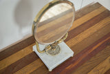 Ornate brass detail and white marble base of a Mid Century Hollywood mirror.