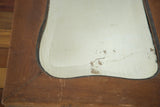 Detail of Art Deco bell mirror's bottom corner, showing wood patina and glass deterioration.