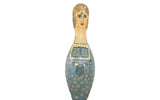 Vintage folk art painted bowling pin of a woman in a blue floral dress, 15.5 inches.