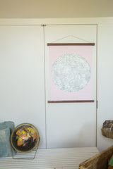 Pink revival moon chart with walnut wood rods hanging on a white door.