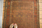 Distressed antique Kurdish rug corner showing muted terracotta, faded blue, and aged geometric patterns.