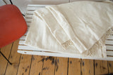 Folded vintage African textile throw, showing natural ivory hand-woven texture and tassels.