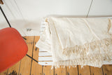 Natural ivory hand-woven African textile throw, highlighting its intricate texture and short tassels.