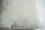 Faded powder blue indigo pillow showing textured fabric and subtle horizontal stripe pattern.