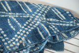 Folded vintage African indigo textile showing ivory striped pattern and a pink stitch.