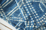 Handwoven African indigo textile with unique ivory patterns, denim blue ground, and visible stitched seams.