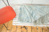Folded hand-woven African textile throw in powder and light blue with long tassels.