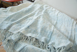 Supple hand-woven textile, highlighting varied powder blue and ivory tones with short tassels.