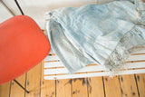 Draped hand-woven African indigo textile with varying light blue hues and short tassels.