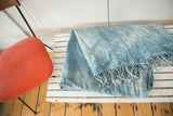 Folded hand woven African indigo textile in varying blues, showing fine texture and short tassels.