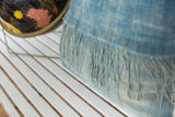 Sun-faded light blue indigo pillow featuring raw, textured fabric and long tassels.