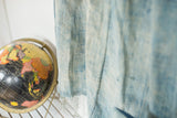 Sun-faded light blue vintage indigo textile texture and fringe beside a globe.