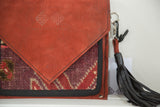 Embossed Swag and Tassel logo on orange suede flap, dark leather tassel, purple red rug.