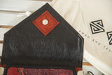 Handmade rug fragment purse's black leather flap with red snap and purple, red textile.
