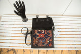 Open dark leather messenger bag, showing geometric antique Kazak rug fragment detail.