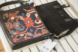 Handmade messenger bag open, revealing dark blue antique Kazak geometric rug fragment and black interior.
