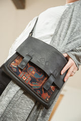 Textured dark leather messenger bag showcasing an antique geometric Caucasian rug fragment.