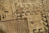 Distressed vintage Caucasian rug corner, showing geometric patterns in earthy brown and camel tones.