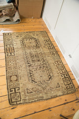 Distressed vintage Caucasian rug corner with geometric brown patterns and textured pile.
