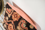 Geometric charcoal pattern of antique Persian rug pillow with soft peach linen backing.