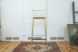 Brass-colored Hollywood Regency stool with criss-cross back and light round seat.