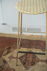 Vintage Hollywood Regency stool with brass legs and a black footrest.