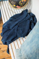 Crumpled dark indigo textile with hand-woven texture and subtle frayed edges.