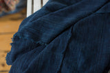 Dark indigo textile throw, revealing intricate hand-woven patterns and a gently frayed edge.