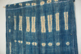 Detail of handmade African indigo textile, showing irregular blue and cream patterns and white stitching.