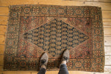 Hand knotted Persian Farahan Sarouk rug corner: dusty red, navy boteh, ivory accents, tattered edges.