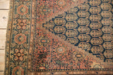 Antique Farahan Sarouk corner, dusty cochineal red border, navy field boteh motif, visible tatter.