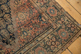 Antique Farahan Sarouk rug's dusty cochineal red field, navy plant motifs, and tattered edge.