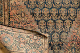 Folded antique Farahan Sarouk rug revealing foundation weave, tattered edge, and navy boteh motifs.