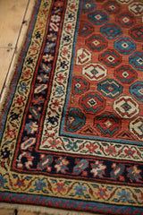 Antique Caucasian rug corner with intricate saffron, navy, and red floral-geometric borders.