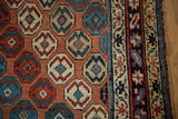 Intricate geometric navy border and blush, red, blue field patterns of a late 19th-century Caucasian rug.