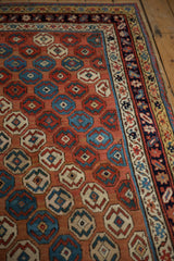 Angled detail of antique Caucasian rug, showing blush field, stylized floral motifs, and detailed borders.