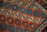 Detail of the antique Caucasian rug's hand-knotted pile, highlighting geometric octagonal motifs in blue, cream, and red.