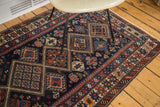 Geometric medallions and pinwheel motifs on dark indigo antique Caucasian rug, featuring rich red and tangerine accents.