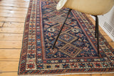 Antique Fine Caucasian rug's corner with tribal geometric patterns, dark indigo field, and white fringe.