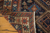 Intricate brick red geometric border, fringe, and indigo field of an antique Caucasian rug.
