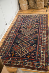 Antique Caucasian rug corner, showing dark indigo geometric field, multiple ornate borders, and fringe.