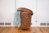 Hand-woven rattan basket showing its partially open lid and draped blue ikat pattern textile.