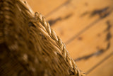 Close-up of the vintage wicker basket's natural light brown braided top edge.