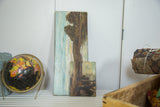 Antique landscape painting showing vertical tree trunk, pale blue sky, and aged texture.