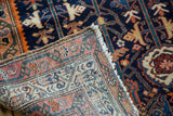 Folded corner reveals antique Malayer rug's hand-knotted geometric weave, fringe, and navy field.