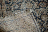 Folded corner of a distressed antique Hamadan rug, revealing dark teal pattern and hand-knotted back.