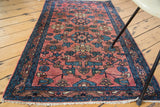 Corner view of antique Lilihan rug with even fringe, repeating blush, teal, and bronze floral motifs.