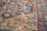 Distressed hand-knotted antique Malayer rug showing golden yellow, navy, and salmon motifs.