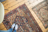 Feet on distressed antique Malayer rug, revealing faded cobalt blue and salmon patterns.